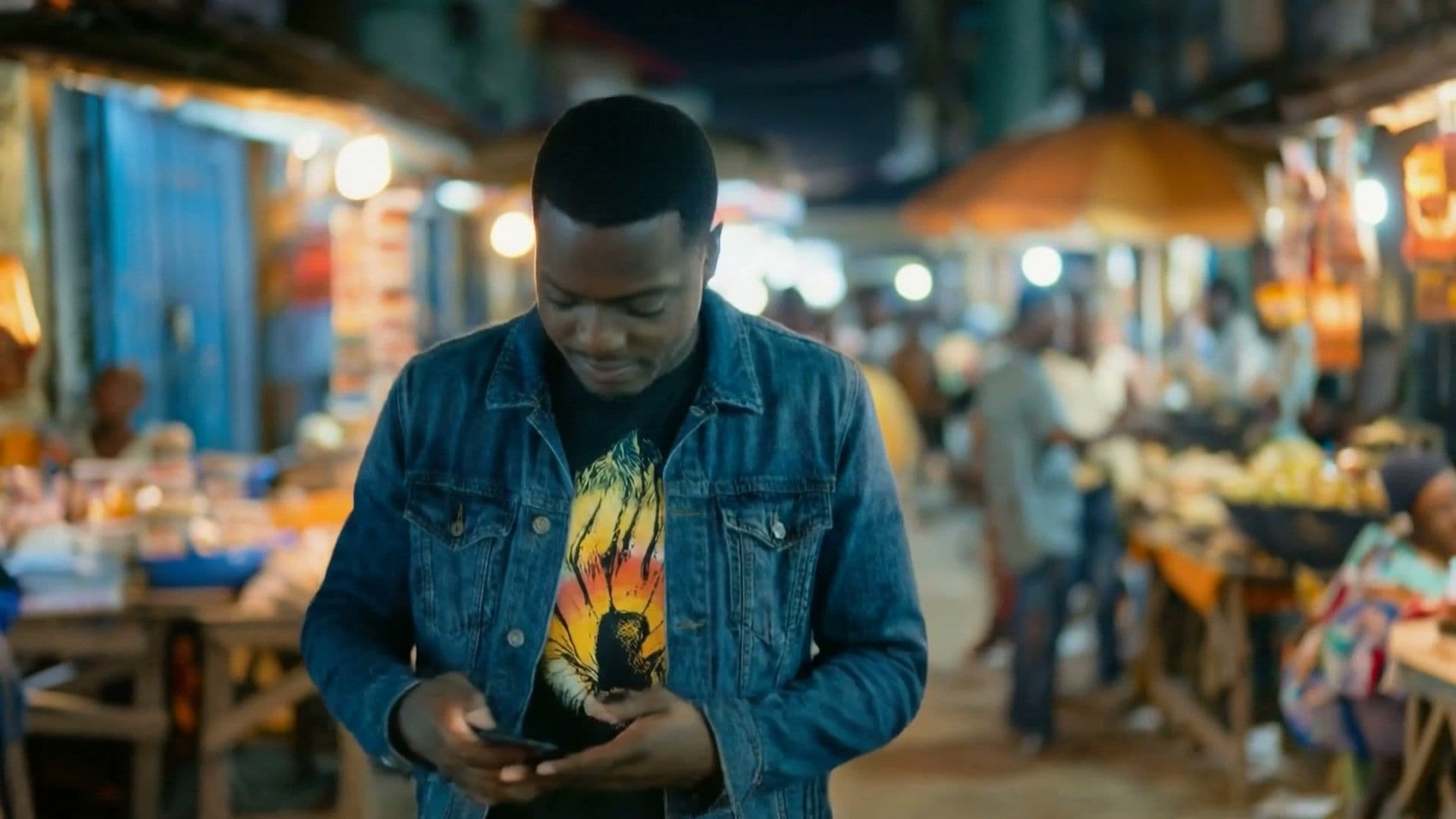 The character in a busy African night market, looking at his phone — the live-action opening